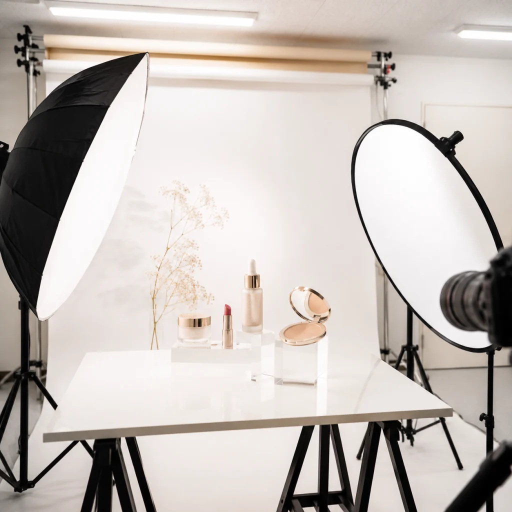 339 - Photo Studio Crit Lab Beauty product shoot setup with makeup items arranged on a white table and two large studio softbox lights in a photography studio.